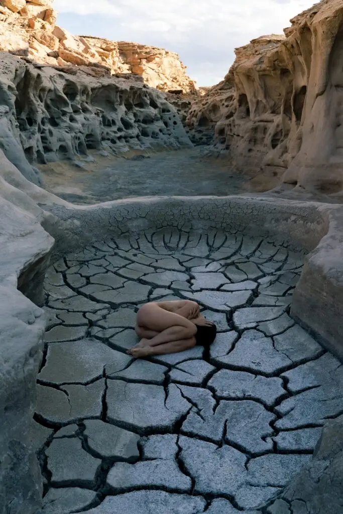Art nude model lying in a cracked dry mud formation, aerial view, Utah desert