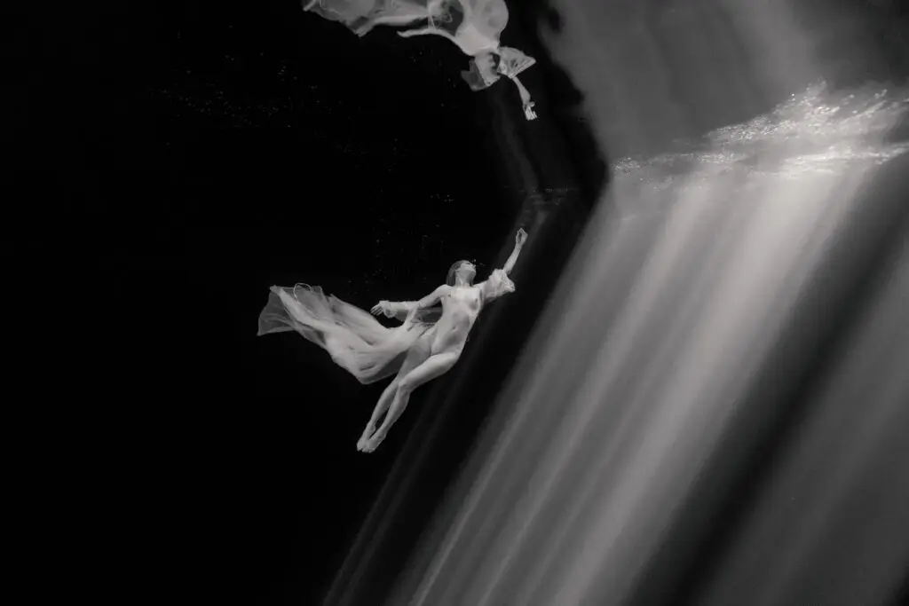 underwater image of model in darkness floating next to a huge beam of light, shot in black and white