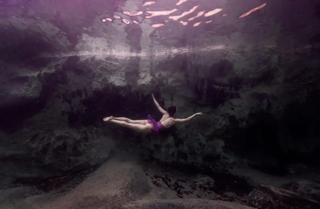 Underwater model in short purple latex dress in dancerly pose in a natural spring