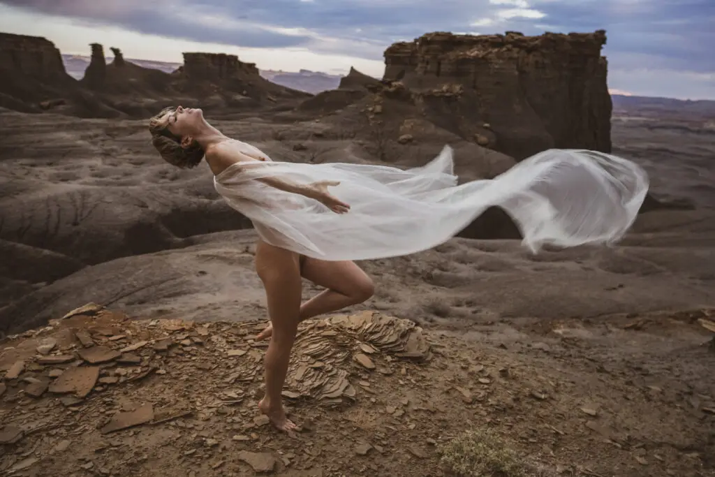 Model clothed in sheer fabric in dancerly back bend pose in the windy utah desert on a dramatic cloudy day