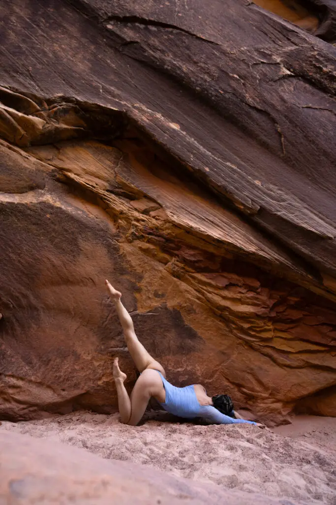 Yoga model in blue bodysuit in angular pose with one leg angled up in the air shot against a utah canyon wall