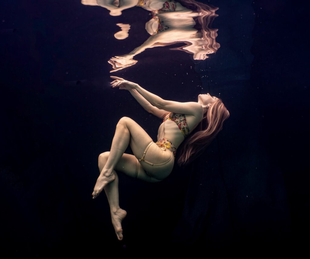 Underwater model in lingerie with long blonde hair floating to the surface with beautiful reflection