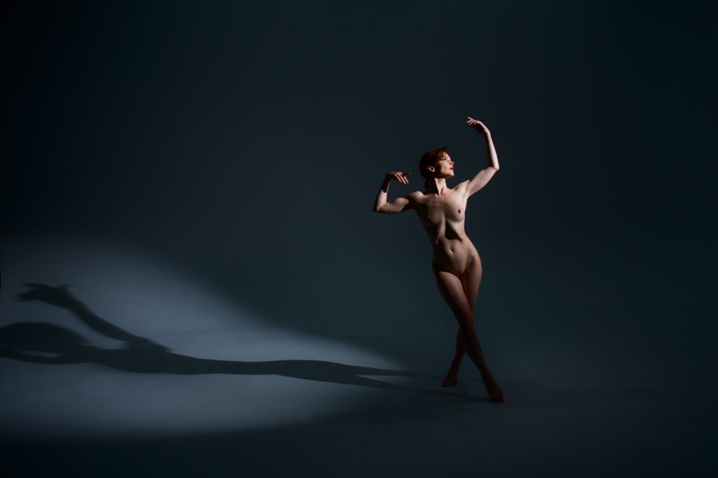Fine art nude model kristy jessica making a dancerly pose with dramatic lighting and long shadows