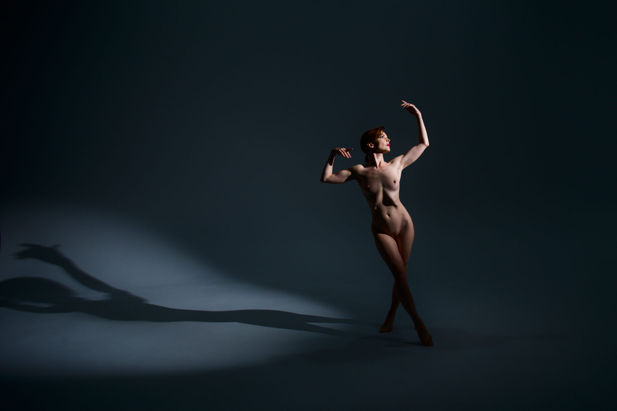 Fine art nude model kristy jessica making a dancerly pose with dramatic lighting and long shadows