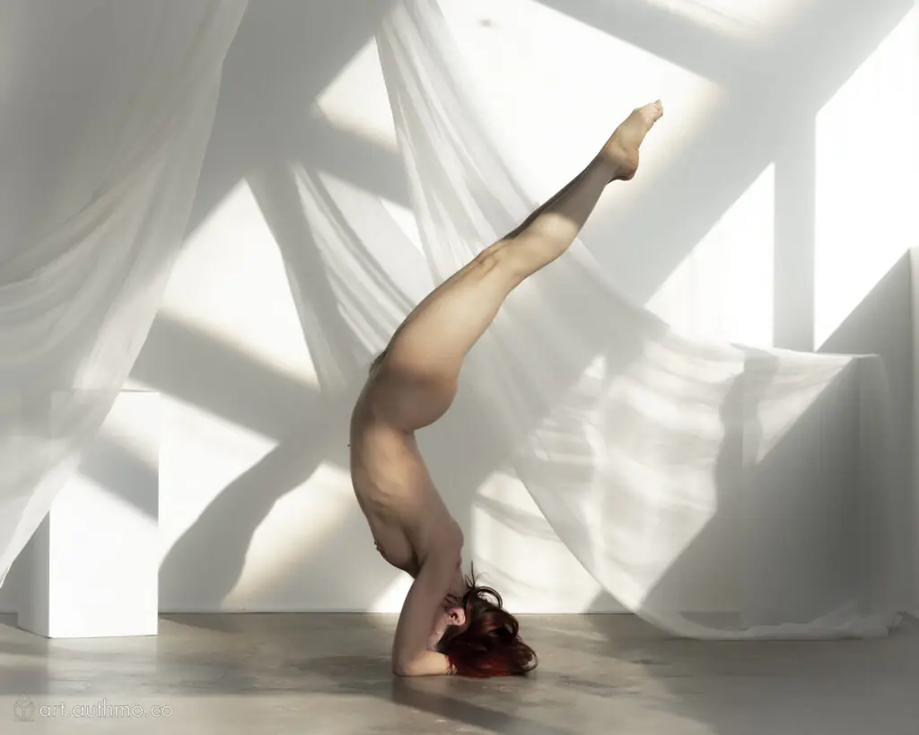 Slender model doing a headstand with legs arching backwards matching the lines on the shadows on the wall