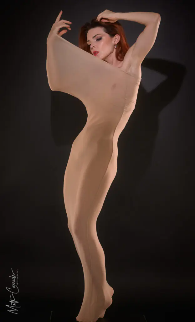 Nude model in stretchy nylon in a dancerly shapely stretched uo pose on a black background