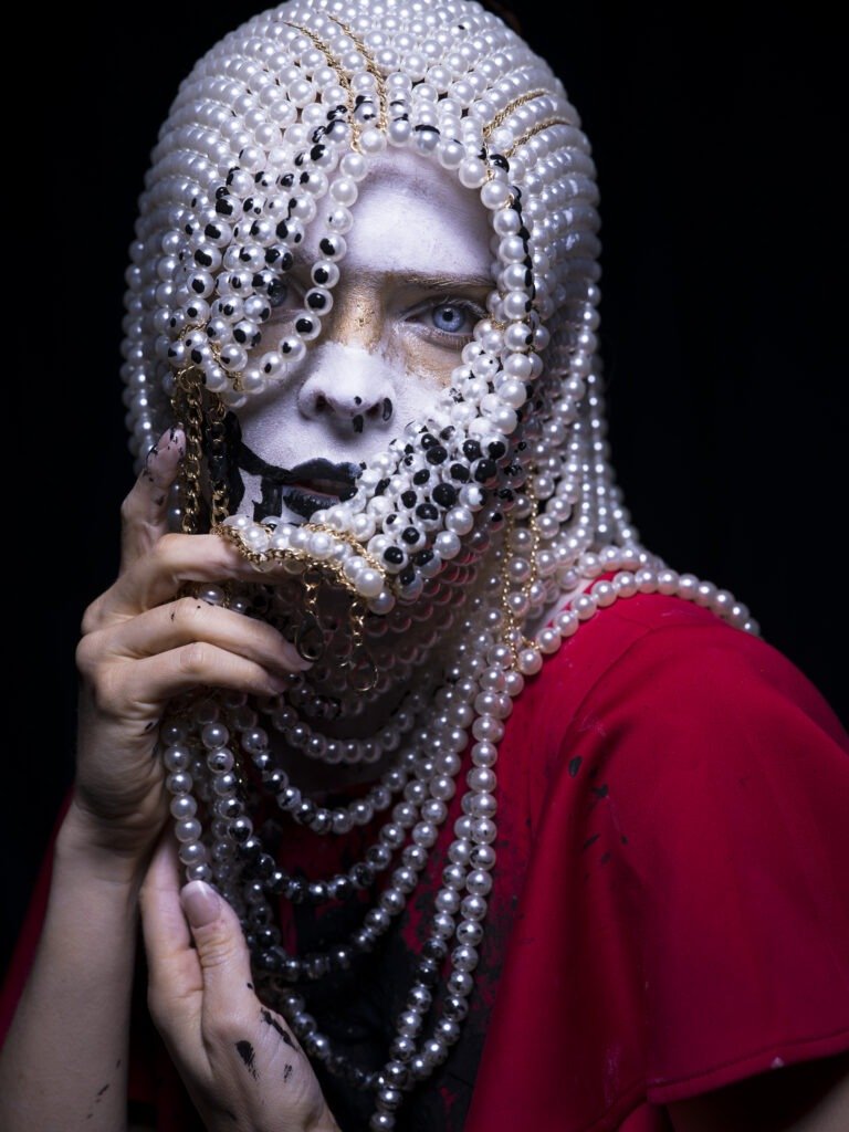 Artistic close up portrait of model with white and gold paint on face wearing headdress of pearls, moody and edgy headshot