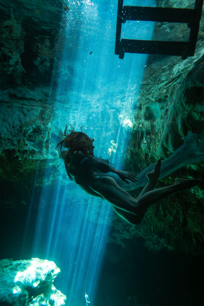 underwater beam of light in an underground spring with a nude model in the foreground swimming towards it